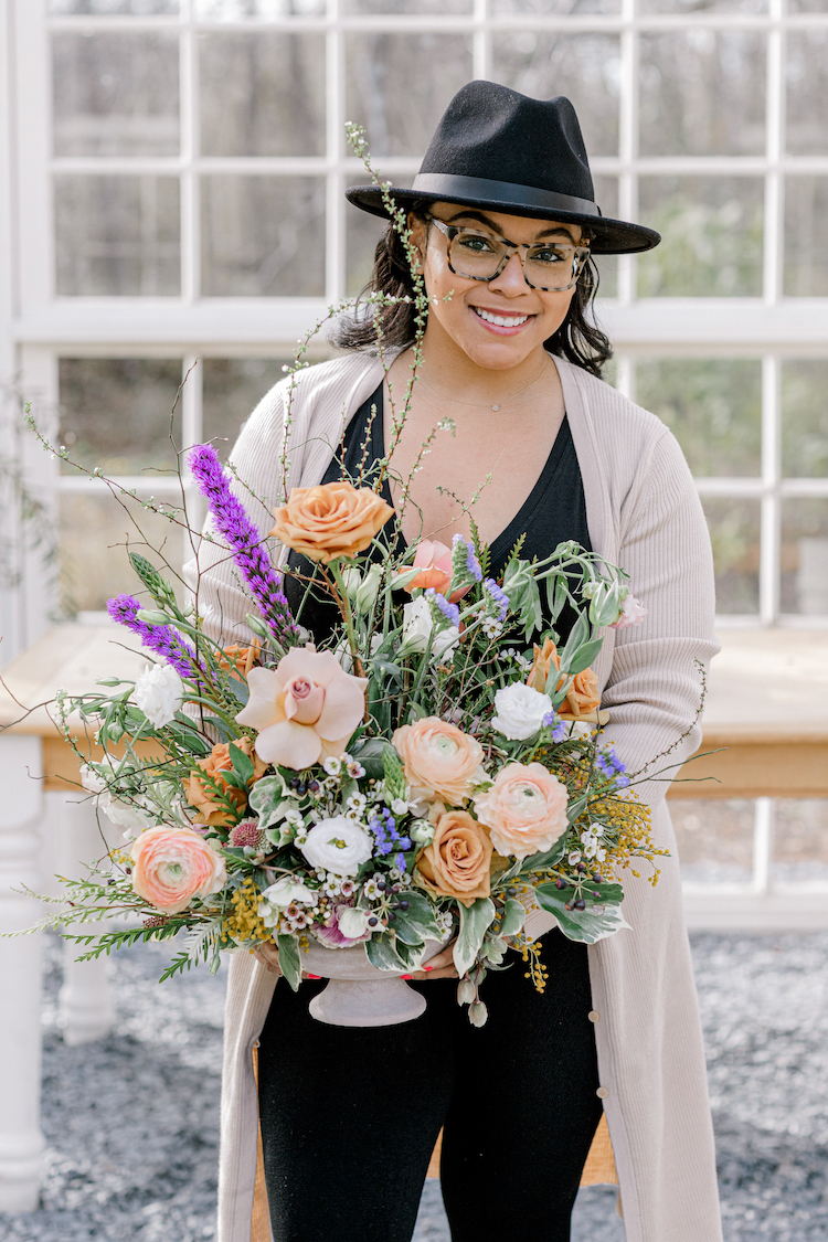 Lauren Hill of Full Bloom by Lauren posing with a lush floral arrangement in an Accent Decor compote.