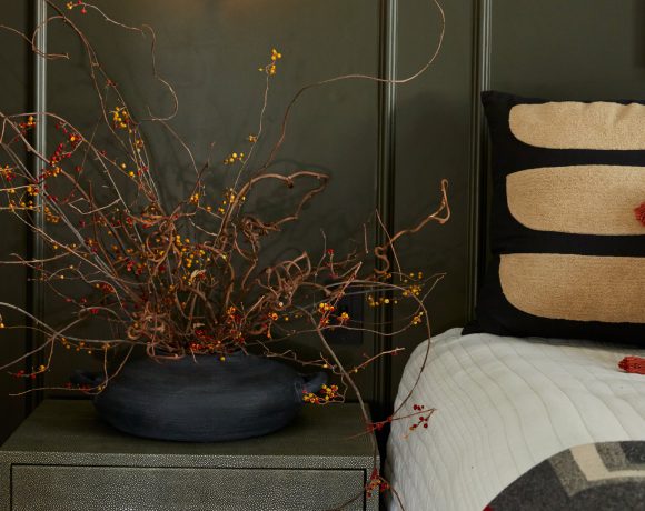 A contemporary floral design featuring a collection of flowers arranged in a sleek, dark container placed next to a bedside.