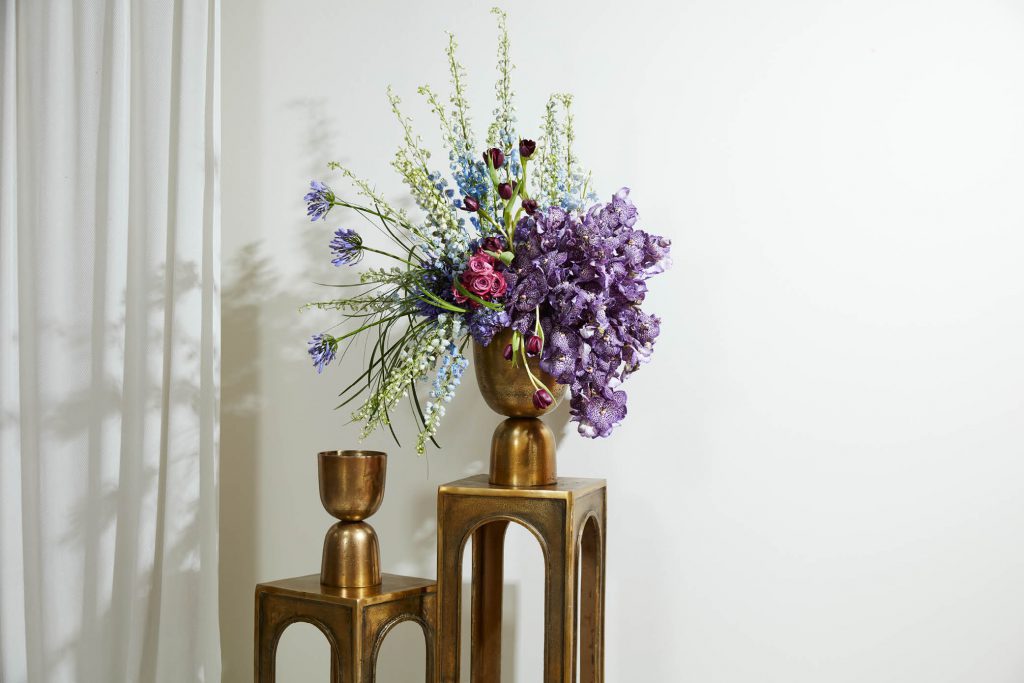  A striking arrangement of purple orchids showcased in a gold vase. The elegant and slender orchid stems rise gracefully from the base, each bearing clusters of exquisite purple flowers with delicate petals. 