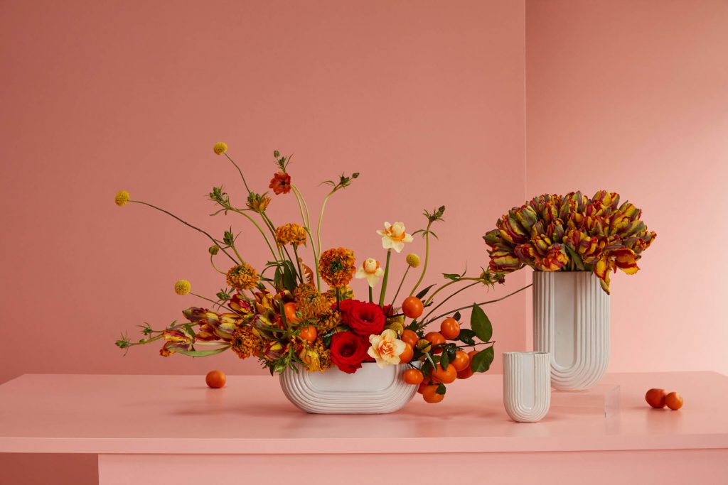 A lovely arrangement of orange flowers displayed in a pristine white vase. The vibrant orange blooms stand out against the crisp white background, creating a visually striking contrast.