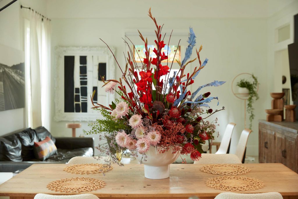 A magnificent large floral arrangement placed in a white vessel, adorning a kitchen island. The arrangement features an abundance of vibrant and diverse flowers, blooming in an array of colors and shapes. 