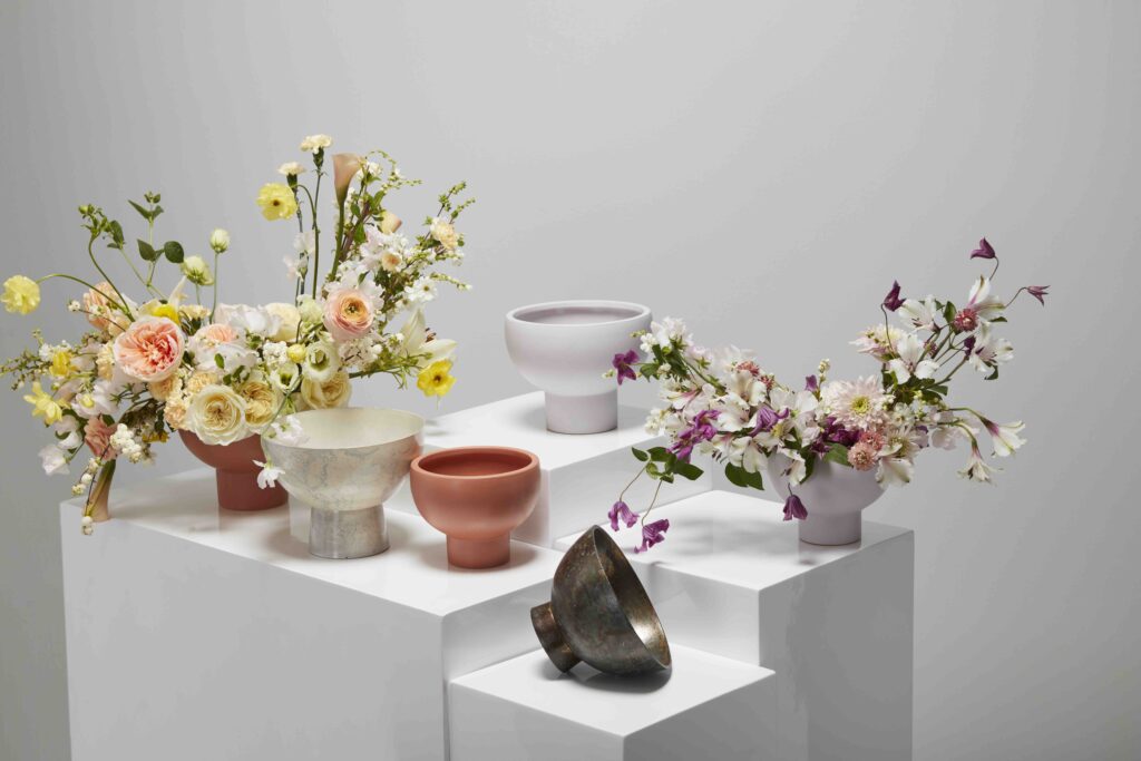 Accent Decor's Eco-Friendly Floral Compotes, filled with flowers, atop white pedestals. 