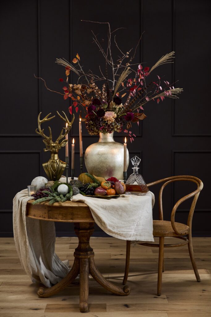 An Eric and Eloise Bust displayed on a table surrounded by a striking, large floral arrangement & candlesticks.