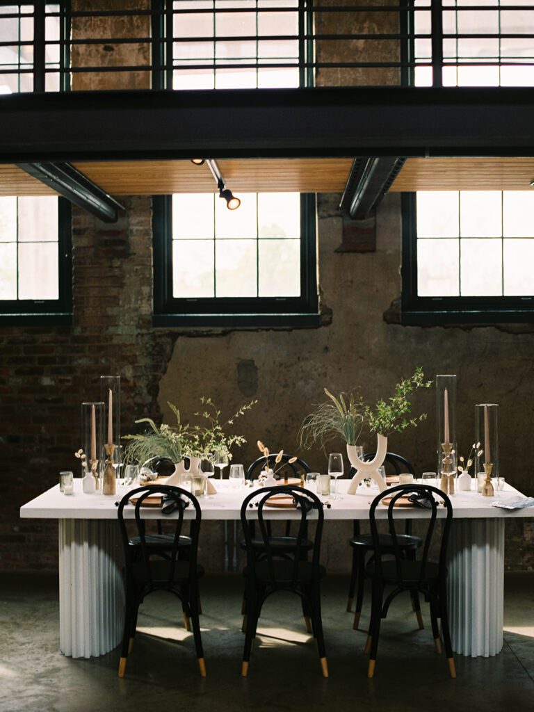 A dramatically decorated white tabletop filled with striking, artful floral arrangements and tall glass sleeves.