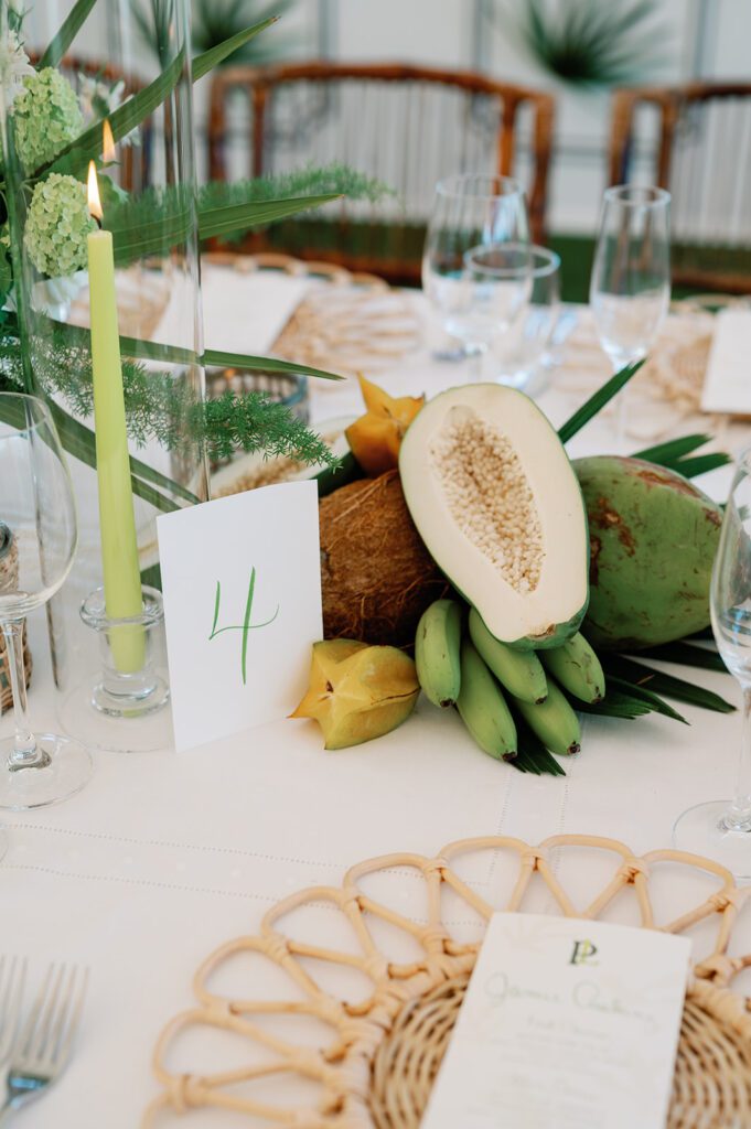 An elegant tabletop decorated with fresh fruit, rattan flatware accents and tall glass sleeves.