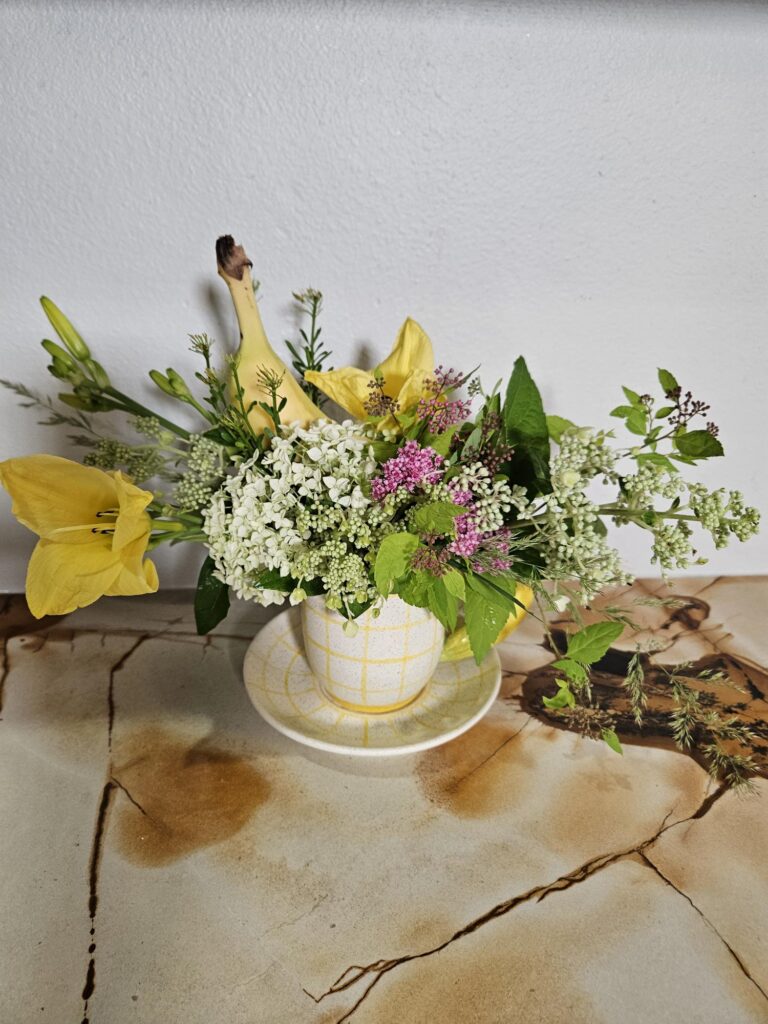 Group shot of a fruit-themed wholesale home decor mug shaped like a banana, styled with flowers.