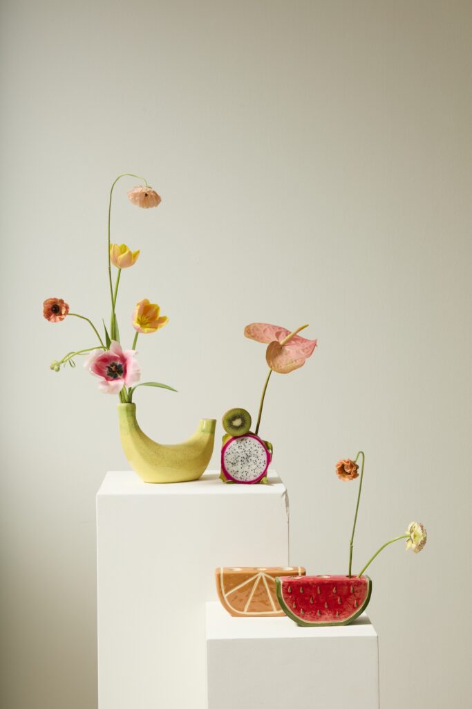 Accent Decor's Banana Budvase, styled with flowers, atop a white pedestal. 