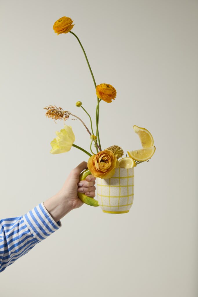 Accent Decor's Fresh Fruit Mug, styled with flowers, held by a outstretched arm. 