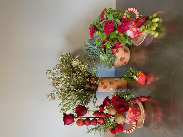 Group shot of fruit-themed wholesale home decor vases and mugs shaped like strawberries, styled with flowers.