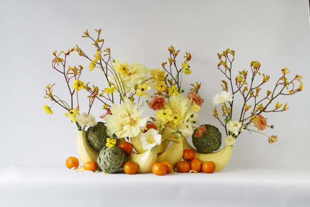 Group shot of fruit-themed wholesale home decor vases shaped like bananas, styled with flowers.