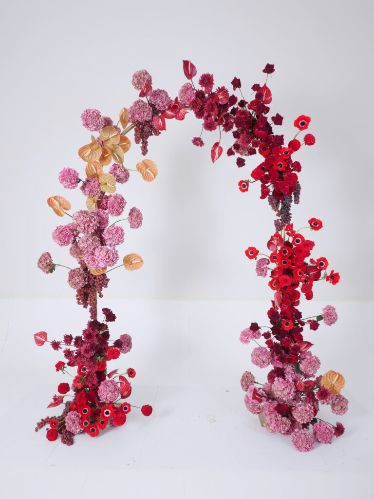 Image of a large arch decor for a wedding utilizing Accent Decor's Soprano Archway. Featured flowers in shades of pink and red.
