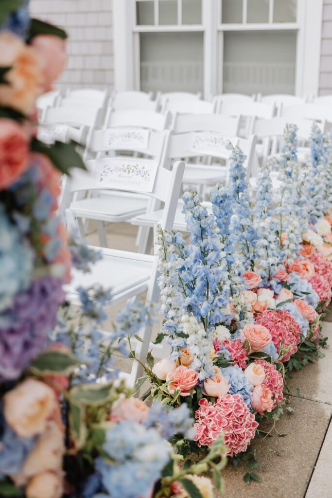 A close-up shot of blue, pink and peach florals designed along a wedding ceremony aisle.