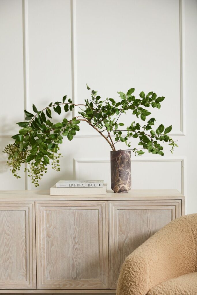 The Accent Decor Calligraphy Vase atop a console table, styled with a fresh green branch and a small stack of books.