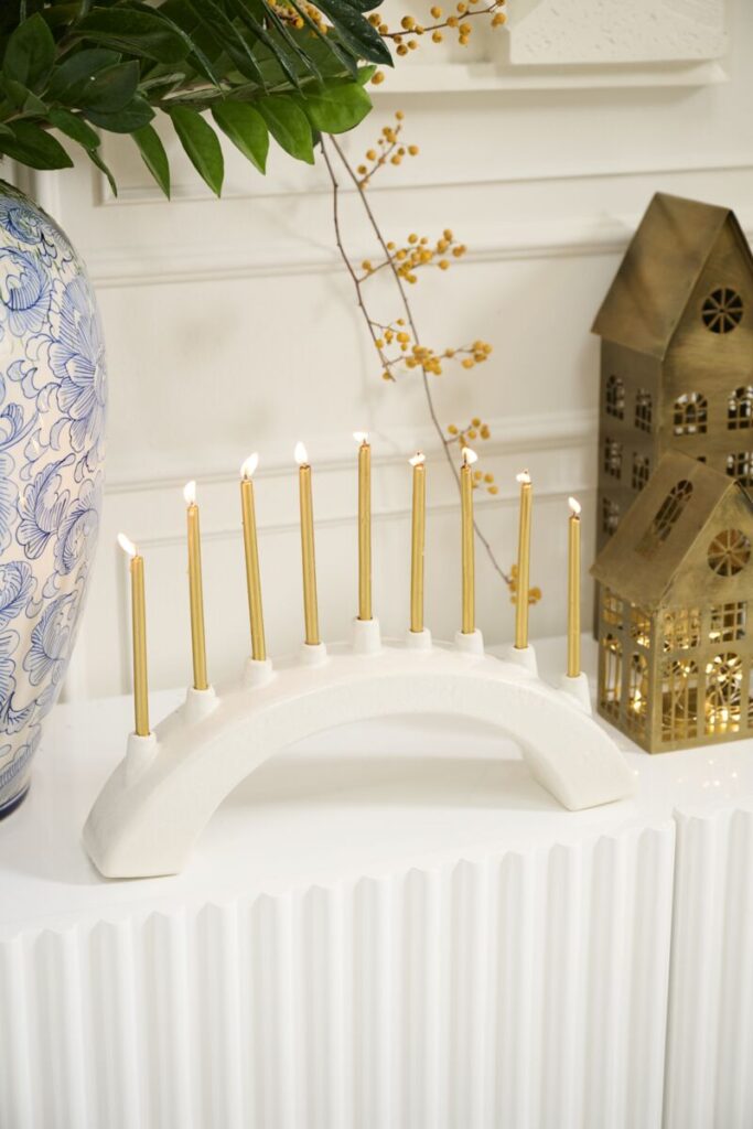 Accent Decor's white Arch Menorah, adorned with traditional Hanukkah candles atop a white table.