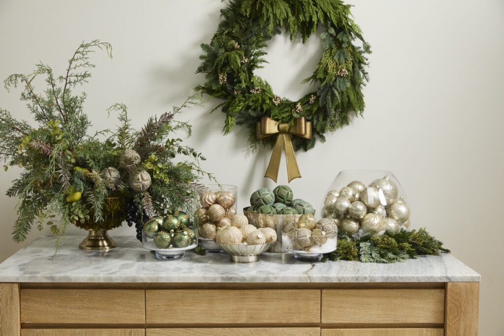 Accent Decor's elegant holiday decor including a wreath, glass vessels filled with ornaments, & greenery styled on a tabletop.