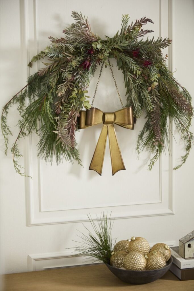 Accent Decor’s Bow Wreath, featuring a brass-colored bow and lush greenery, mounted on a white wall.