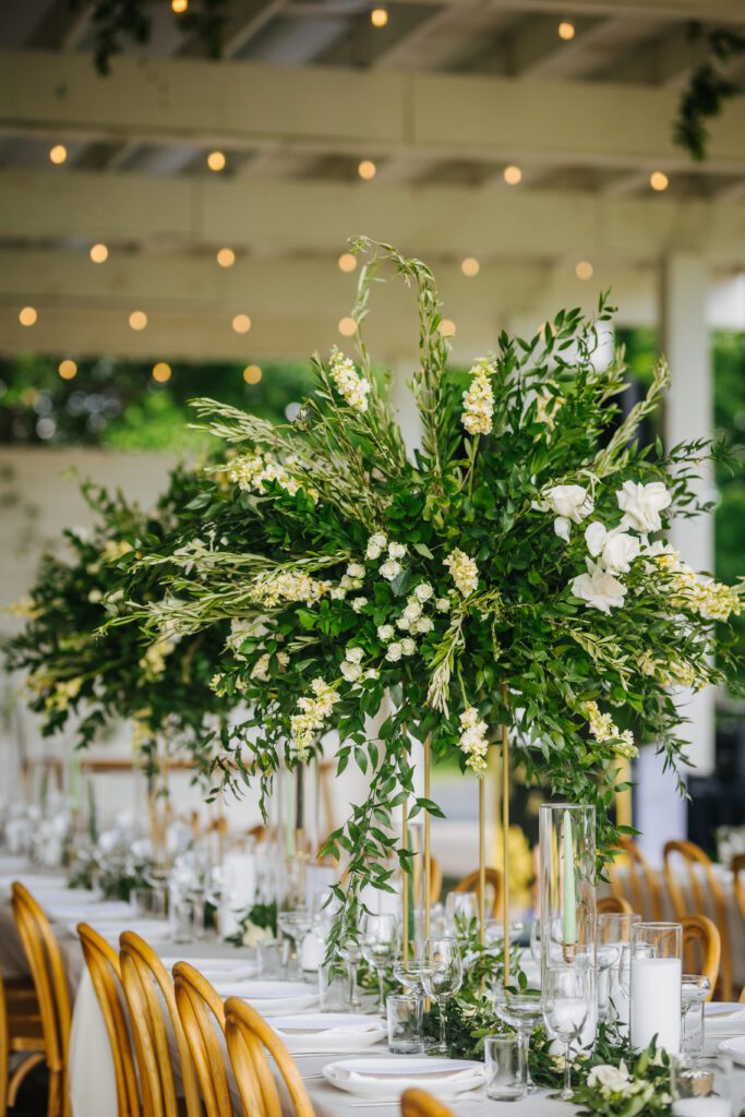A beautifully decorated wedding reception tablescape ft. white linens, large glass vases, glassware, florals and greenery.