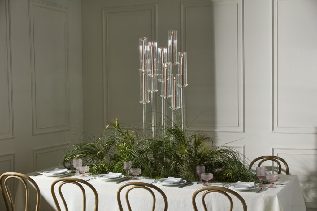 An elegantly styled tablescape featuring a grass-inspired centerpiece with wholesale event decor including candlesticks, glass drinkware and flatware.