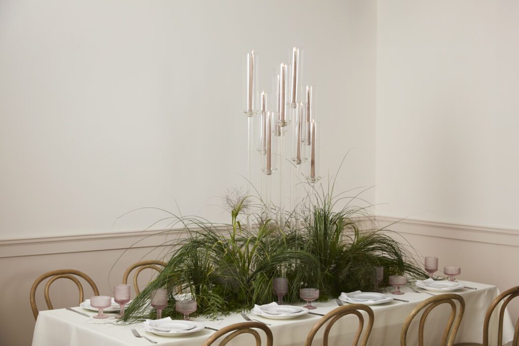 An elegantly styled tablescape featuring a grass-inspired centerpiece with wholesale event decor including candlesticks, glass drinkware and flatware.
