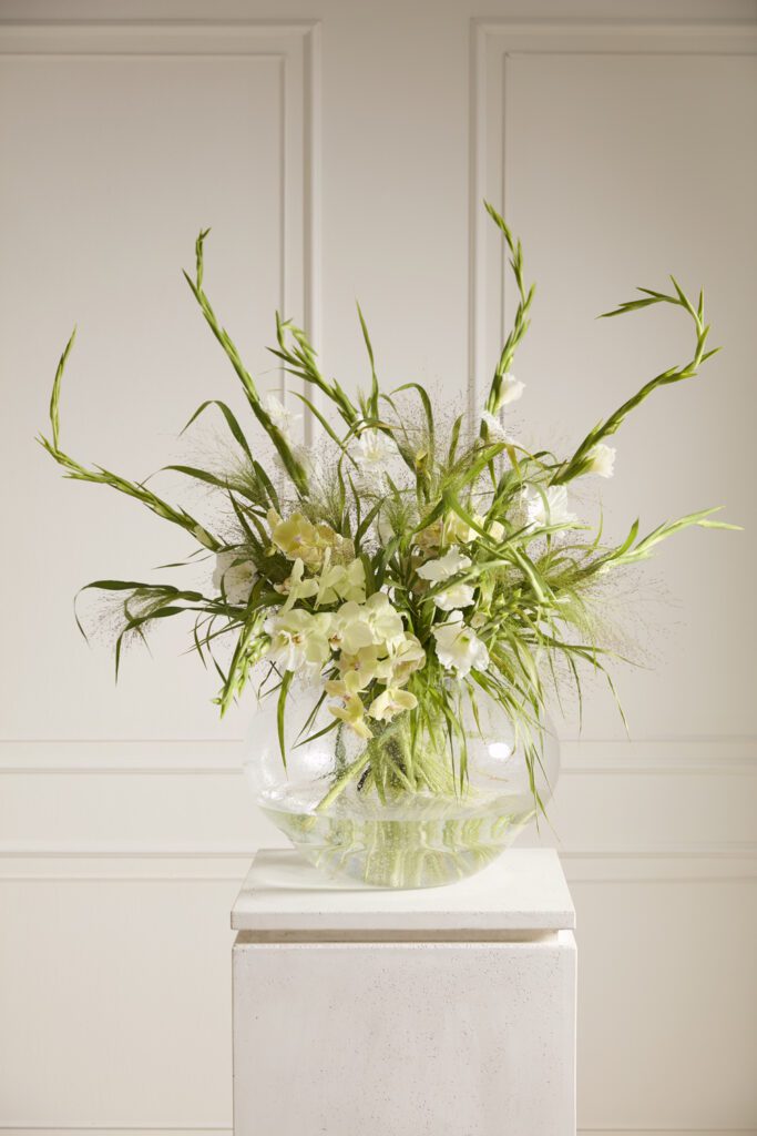 Accent Decor's Bala Vase, a large glass vase, artfully styled with florals atop a white pedestal.