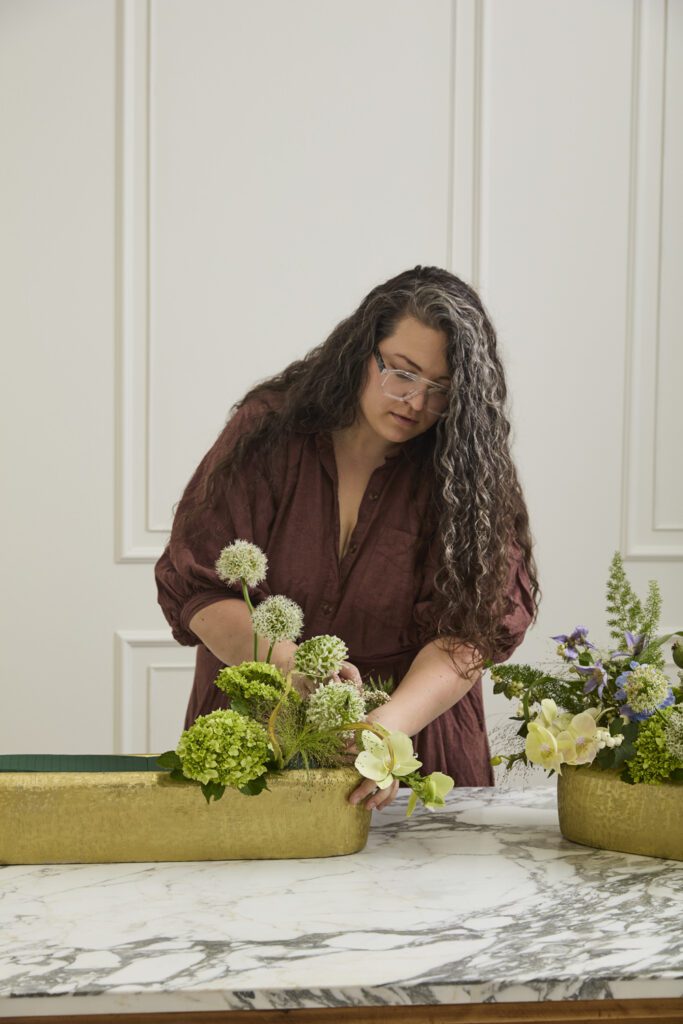 Image of a woman arranging florals into the Blaze Trough, a decorative trough, offered by wholesale decor supplier, Accent Decor.