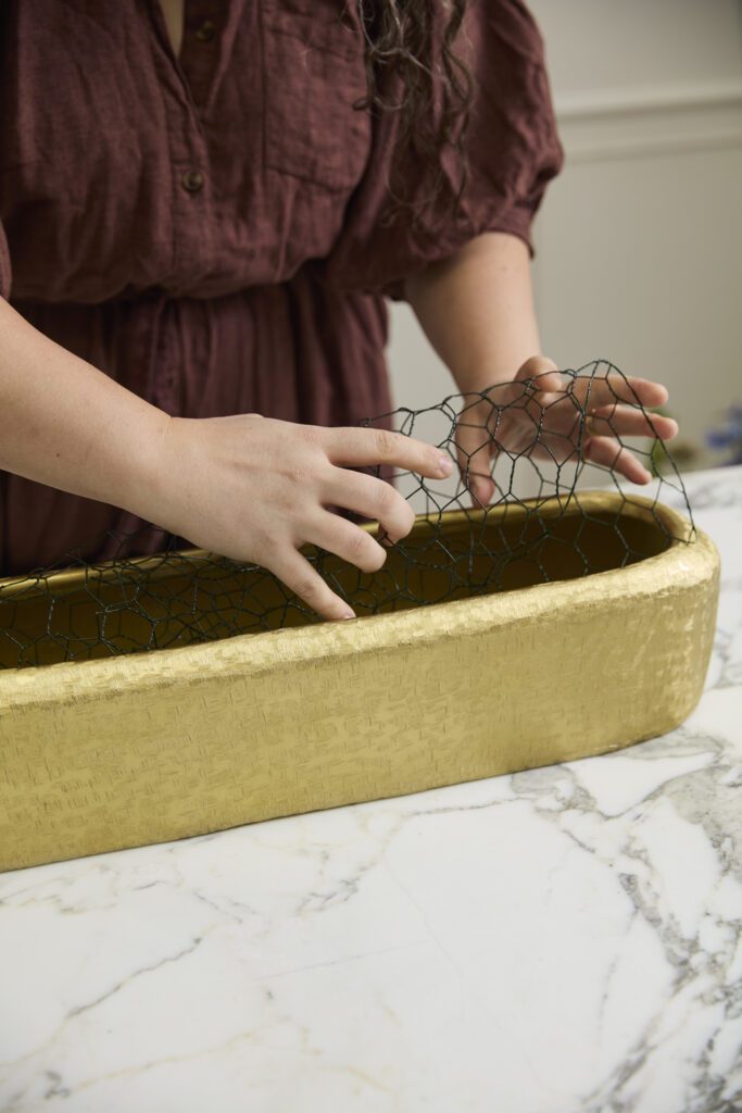 Image of hands manipulating chicken wire into the Blaze Trough, a decorative trough, offered by wholesale decor supplier, Accent Decor.