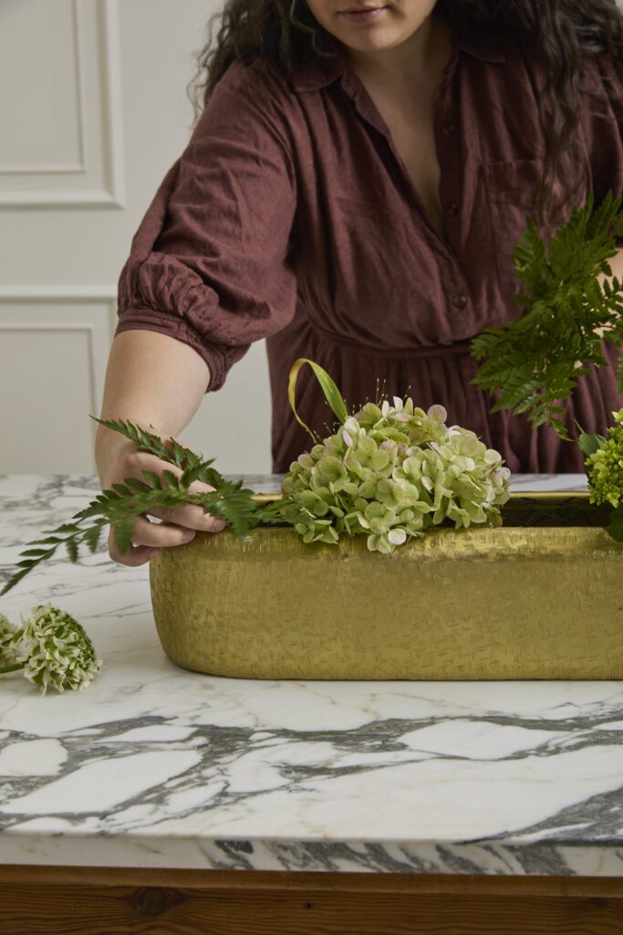 Image of hands arranging florals into the Blaze Trough, a decorative trough, offered by wholesale decor supplier, Accent Decor.
