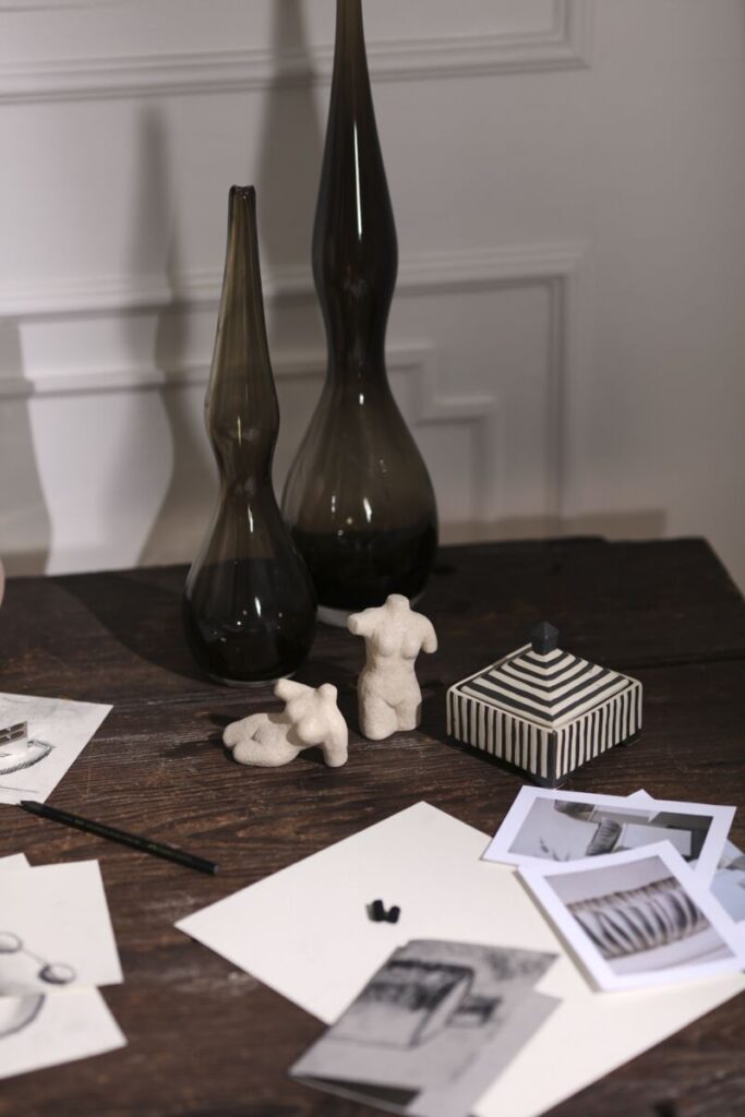 A desk featuring a spread of decorative objects, including 2 small sculptures of the female form, and scattered photos and papers.