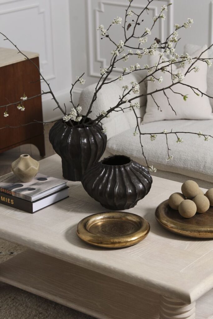 A stylish coffee table topped with various wholesale home decor accents including trays, coffee table books and 2 large black vessels.