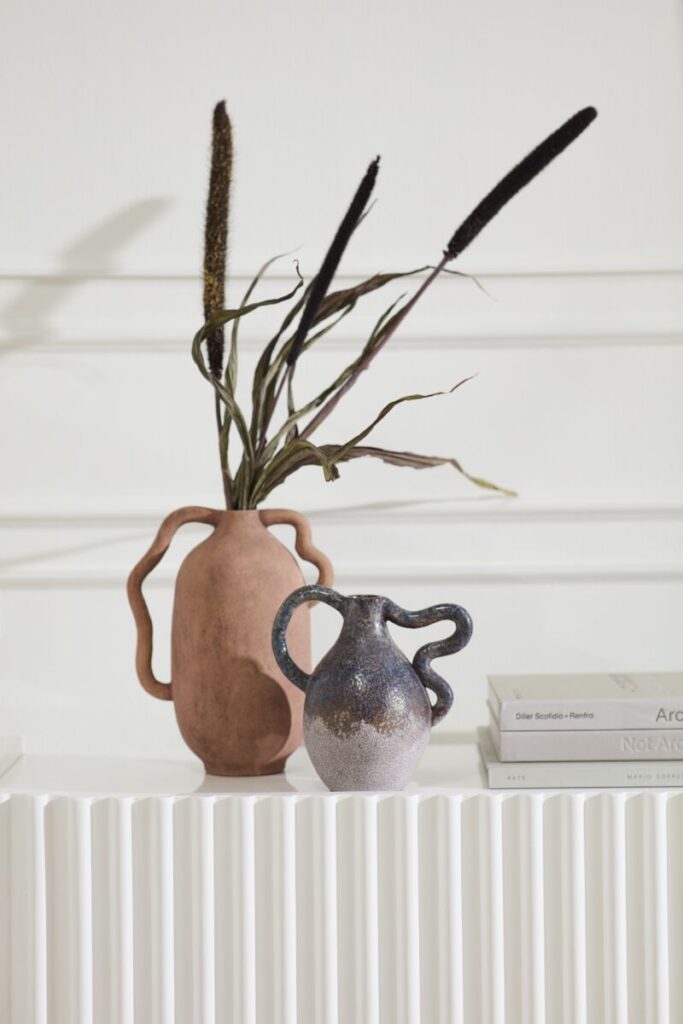 Two striking vessels, one terracotta the other a smokey graphite, sitting atop a stylish console table.
