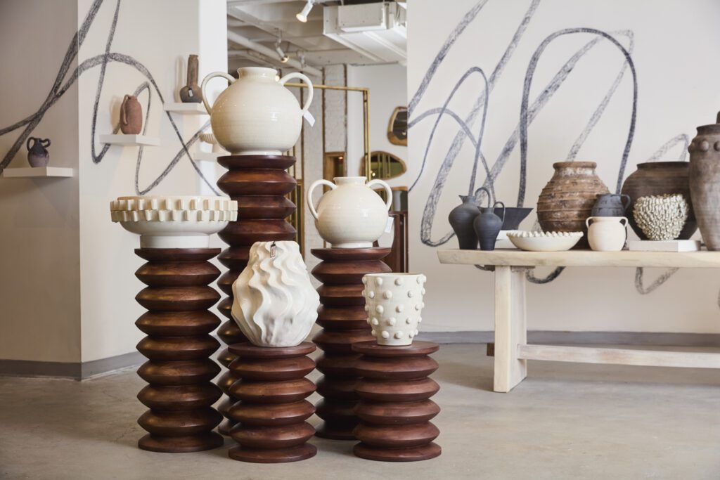 Image of colorful white planter pots, bowls, vases & home decor on a variety of tables against a white wall.