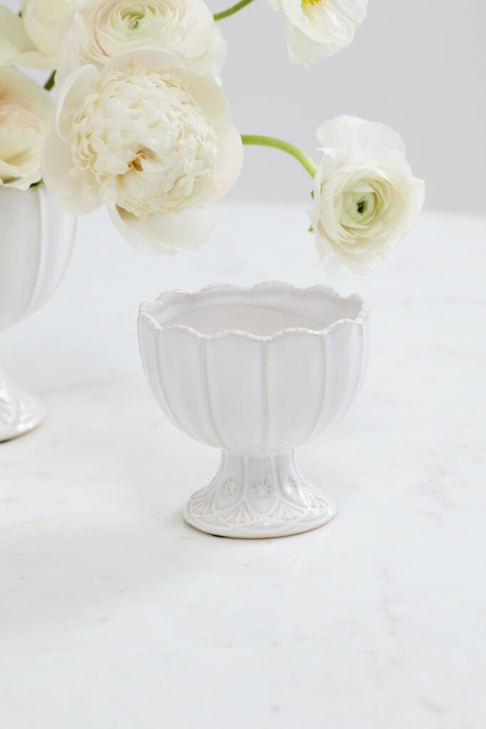 A scalloped wholesale vase atop a white tabletop containing white, lush florals.