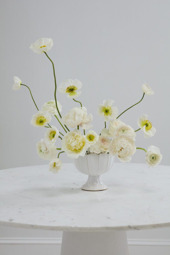 A scalloped wholesale vase atop a white tabletop containing white, lush florals.