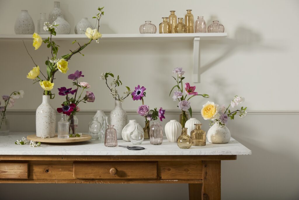 Variety of glass and ceramic vases and budvases, styled with flowers, on a floral workshop table.