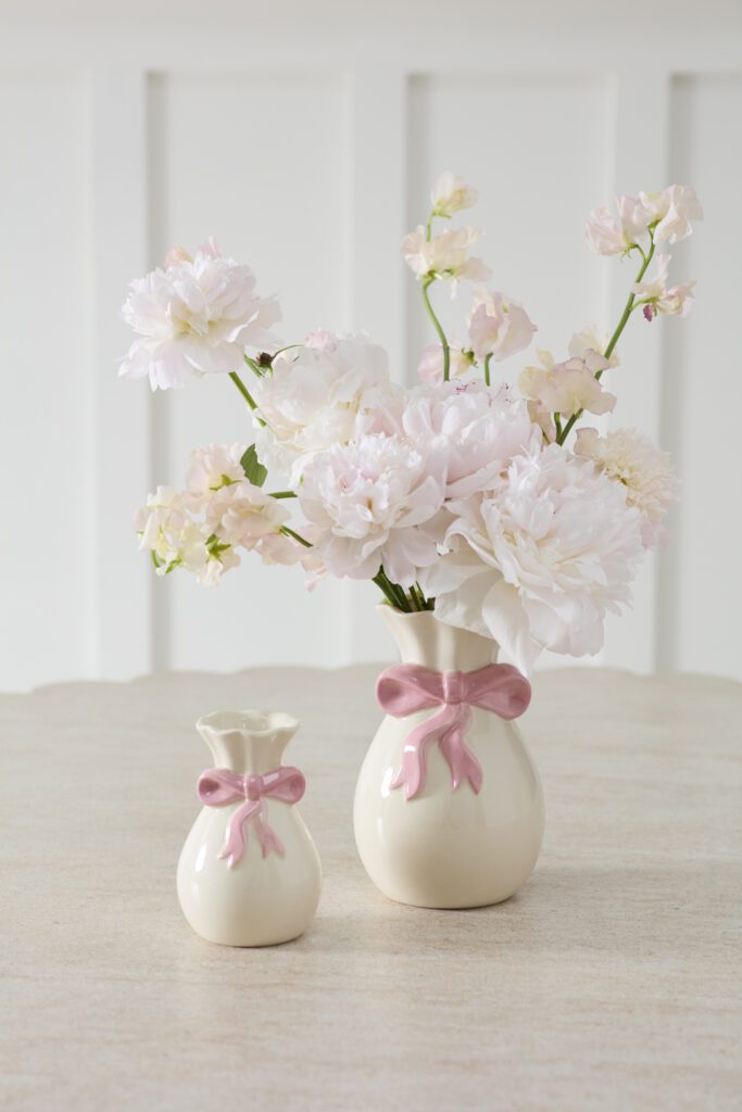 White ceramic vase with a pink bow on a white tabletop.