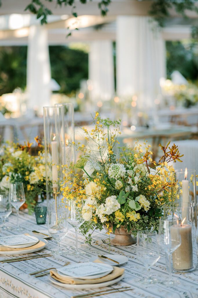 An event tabletop styled outdoors with lush, fresh flowers and wholesale event decor including votives, candles & flatware.