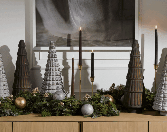 A decorated console table adorned ceramic seasonal decor items including ceramic trees, candlesticks, ornaments and greenery.