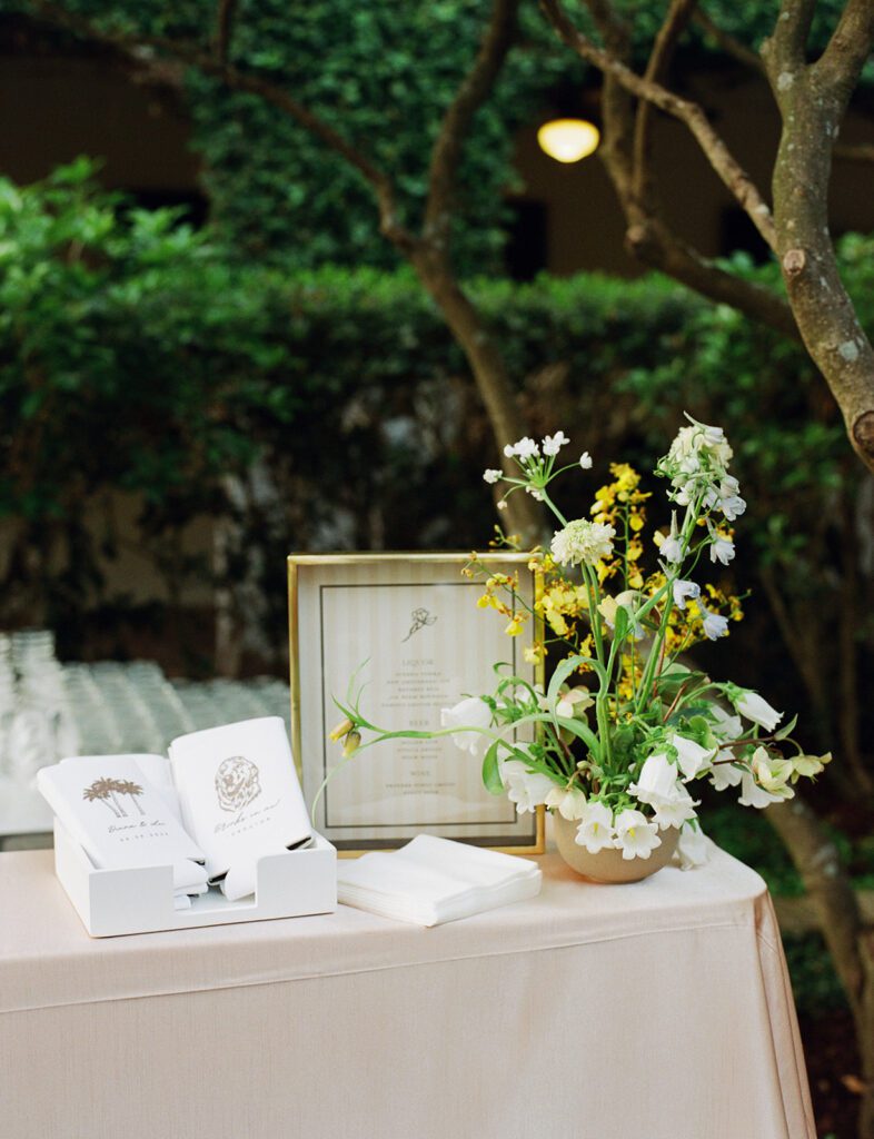 An event tabletop styled outdoors with fresh, colorful flowers and playful wholesale event decor including drink koozies and custom napkins.