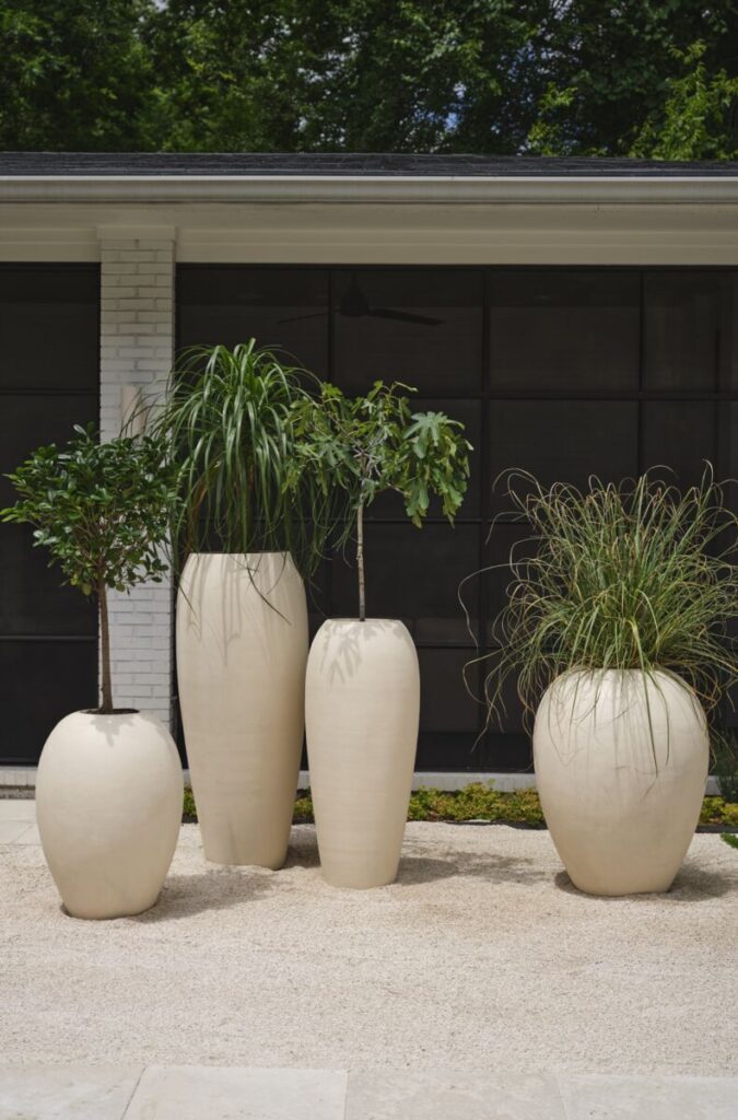 Assortment of large outdoor planter pots in taupe, neutral tones styled in a backyard.