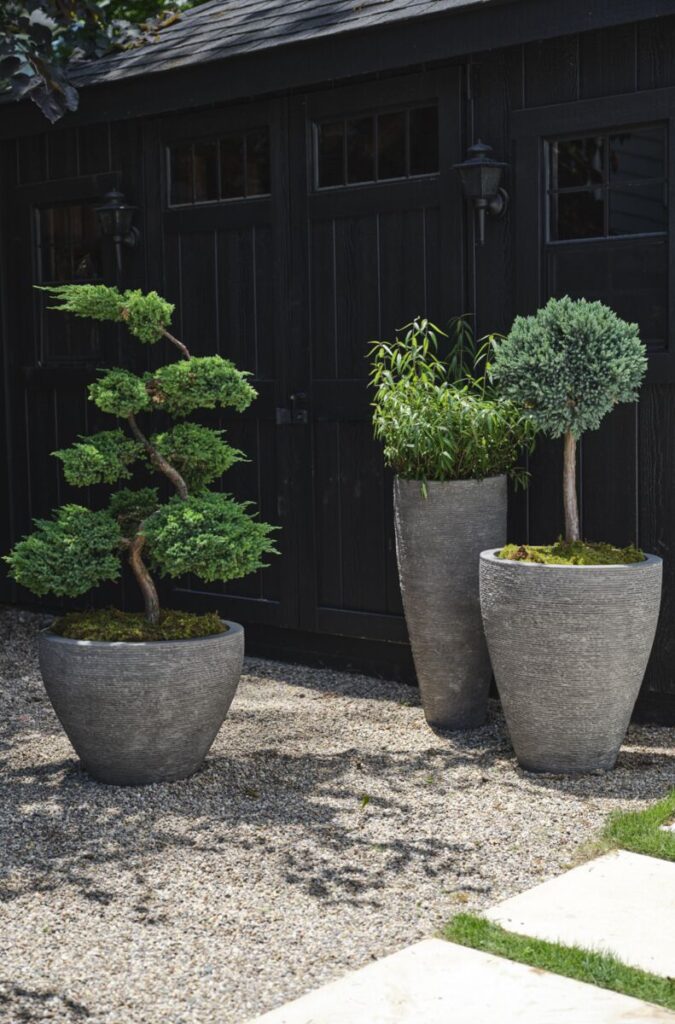 Assortment of large outdoor planter pots in gray, neutral tones styled in a backyard.