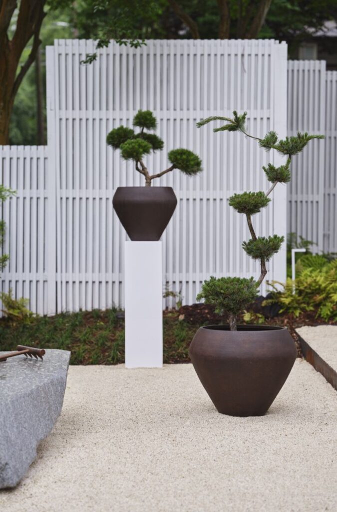 Assortment of large outdoor planter pots in black, neutral tones styled atop a pedestal in a backyard.