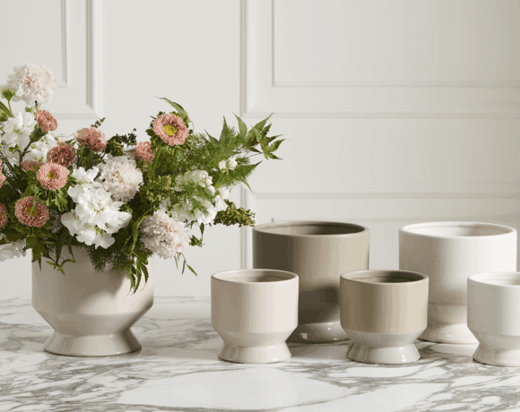 Ceramic pots atop a table, with one featuring a lush floral arrangement.