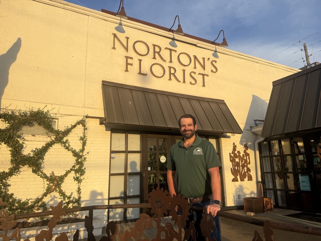 The exterior of a floral design studio with a smiling man at the entrance.