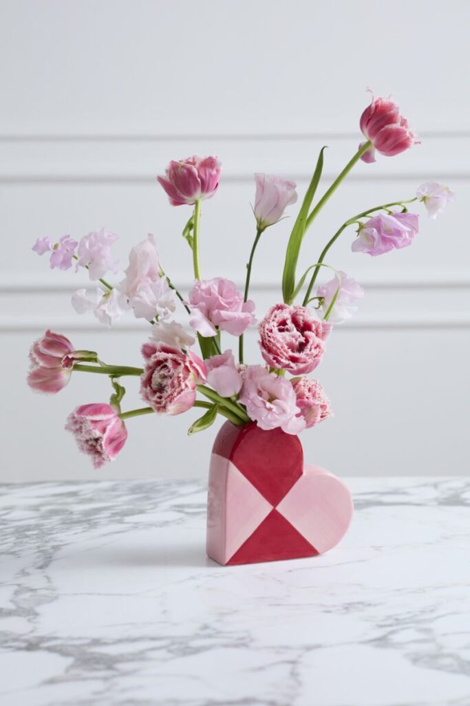 A heart-shaped budvase in the shape of a heart filled with a simple and striking floral arrangement.