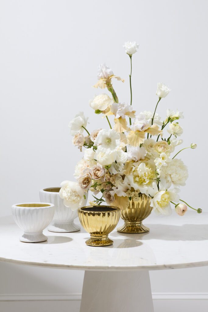 Gold Coronation Compote filled with white florals atop a while tabletop.